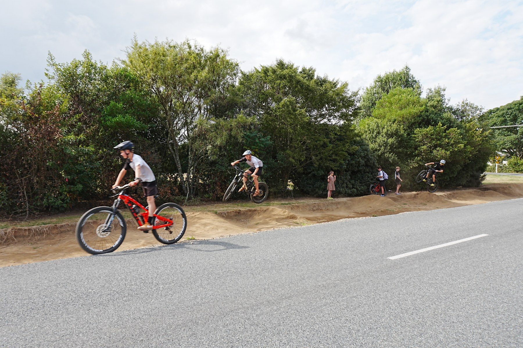 Pirongia children riding bikes on the road verge on the corner of McClure and Belcher Streets.