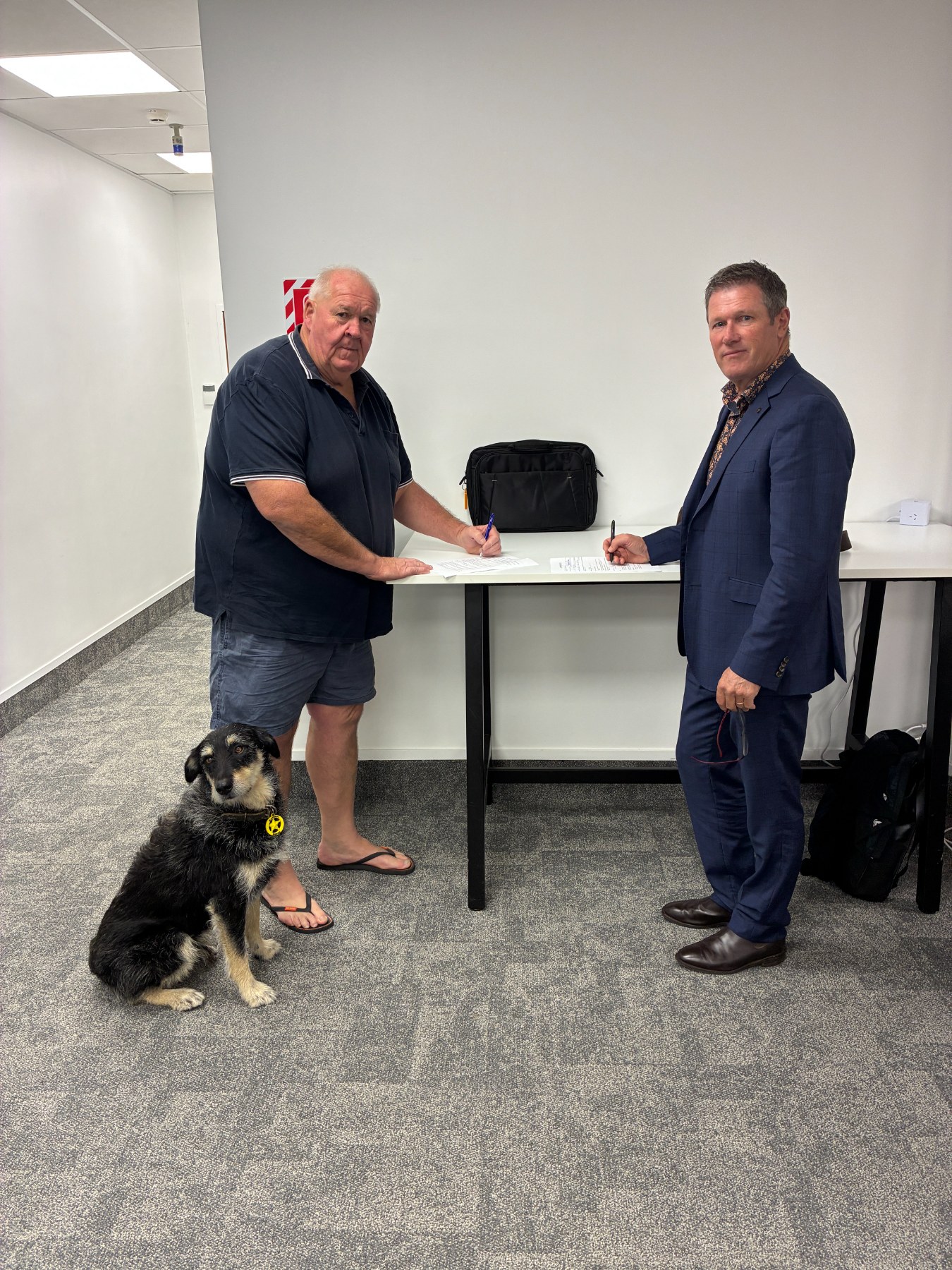 Ōtorohanga Mayor Rodney Dow (left) and Waipā Mayor Mike Pettit (right) sign their district states of emergency with Ōtorohanga Mayoral Dog Zeb.
